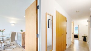 A modern interior with a dining area, wooden doors, and a hallway leading to another room. - Deluxe Two Bed Fully Serviced Apartment in ExCeL (London)