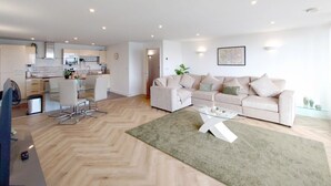 A modern living room with a sofa, coffee table, and a dining area with chairs. - Deluxe Two Bed Fully Serviced Apartment in ExCeL (London)