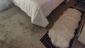A modern bedroom with a large bed, a white furry rug, and a view of greenery through a window. - The River Condos - Detroit, Michigan (Detroit)