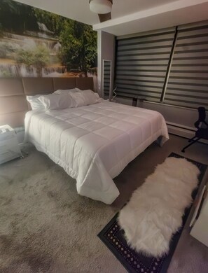 Ein modernes Schlafzimmer mit einem großen Bett, einem flauschigen weißen Teppich und Blick auf Grün durch ein Fenster.
