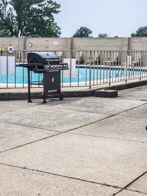 Ein Grill in der Nähe eines Schwimmbeckens mit Liegestühlen und einer Ziegelwand im Hintergrund.