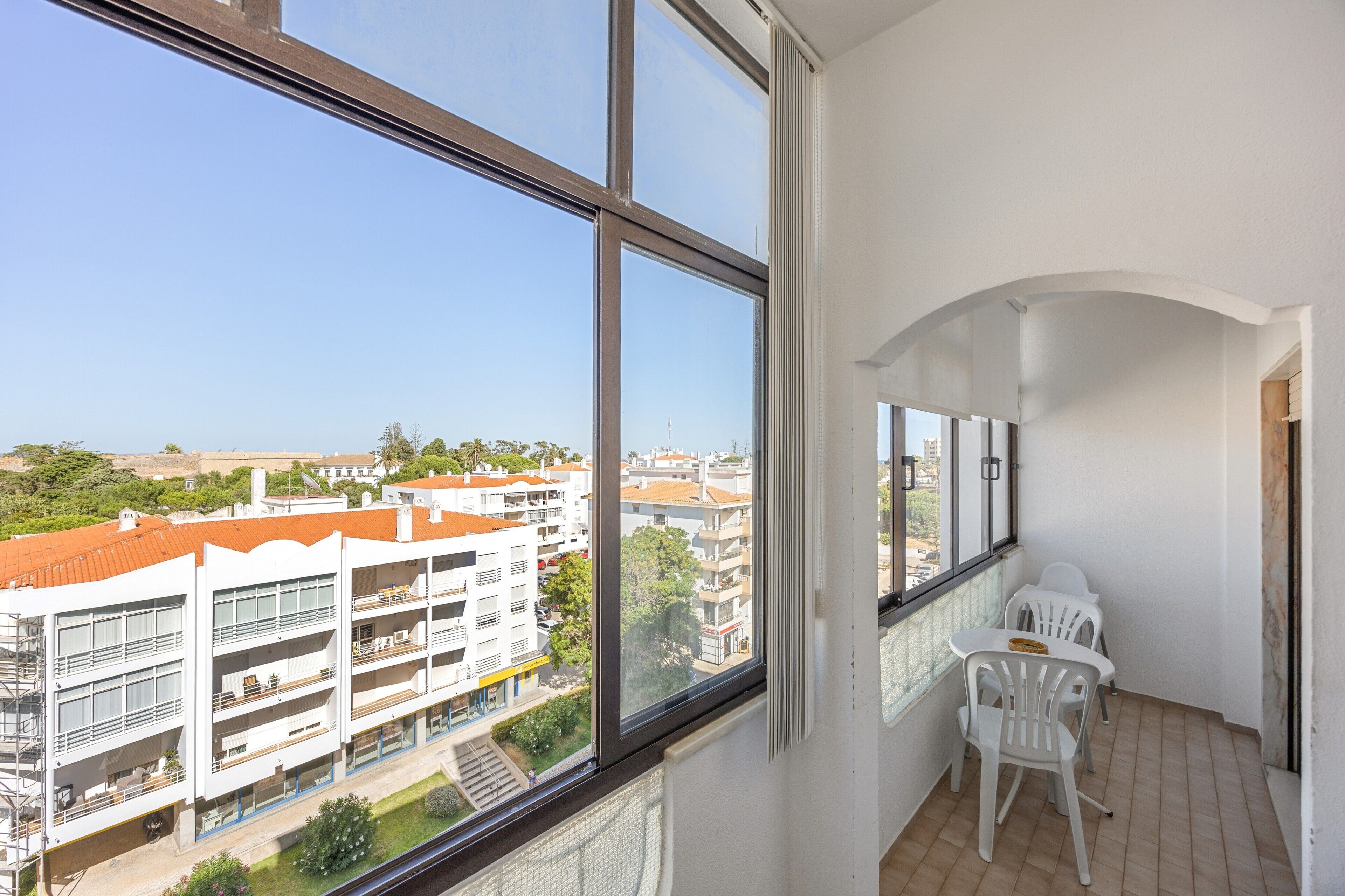 Un balcon donnant sur un paysage urbain, des murs blancs et une petite table avec des chaises.