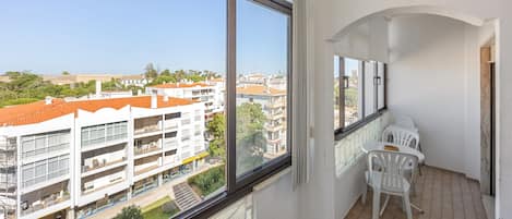 Uma varanda com vista para a cidade, paredes brancas e uma pequena mesa com cadeiras.