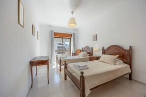 A hotel room with two beds, a desk, and a window with curtains. - Apartment 'Central  - Lagos' with Sea View, Balcony and Wi-Fi (Lagos)
