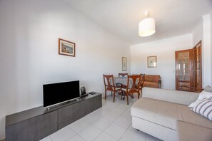 Ein Wohnzimmer mit Flachbildfernseher, einer Couch, einem Esstisch mit Stühlen und einer Holztür.