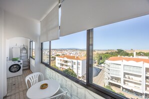 Ein Balkon mit Blick auf eine Stadtlandschaft, einer Waschmaschine und einem Tisch mit Stühlen.