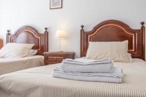 Quarto de hotel com duas camas, cada uma com cabeceira de madeira, mesa de cabeceira com abajur e toalha dobrada na cama.