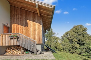 A wooden building with a sloped roof, a wooden staircase leading to a porch, and a pile of firewood outside. - Bed and Breakfast 'Formigher' with Mountain View and Wi-Fi (Limana)