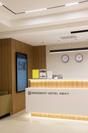 Tauleller de recepció amb un rellotge, un pantalla digital i un cartell per a l'Hotel Resident Abay.