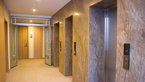 A hallway with two elevators, carpeted floor, and wooden doors. - Resident Hotel Abay (Almaty)