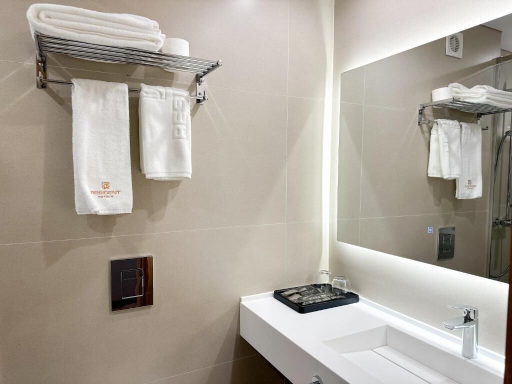 A modern bathroom with a white sink, a large mirror, and a towel rack with folded towels.