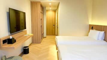 Habitación de hotel con una cama, televisor, armario de madera, un pequeño rincón de descanso y un pasillo que conduce a otra habitación.