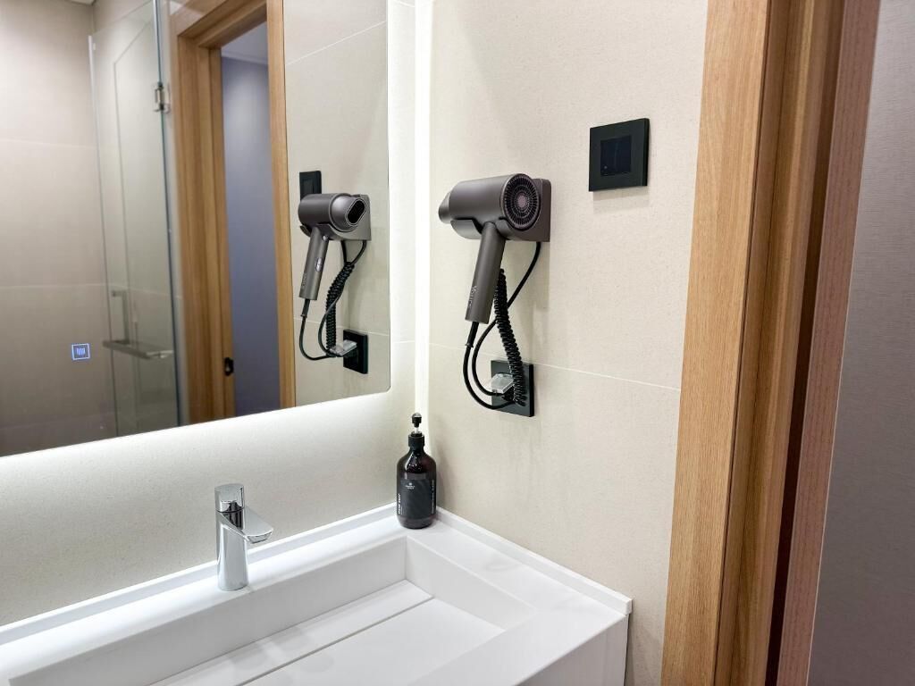 A bathroom with a white sink, a mirror, and two wall-mounted hair dryers.