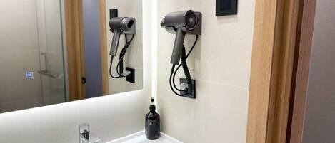 A bathroom with a white sink, a mirror, and two wall-mounted hair dryers.