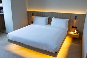 Habitació d'hotel moderna amb llit, taules de nit i capçal de llit integrat.