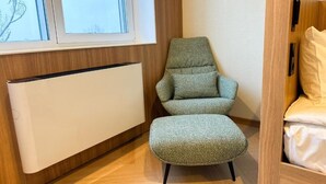 A room with a bed, a green upholstered chair, a radiator, and a window with a view of trees. - Resident Hotel Abay (Almaty)