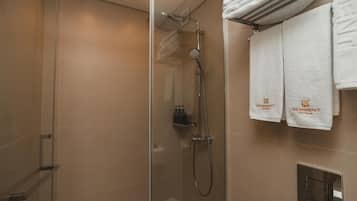 Un área de ducha con paredes de vidrio, un perchero con dos toallas y un panel de control en la parte inferior.
