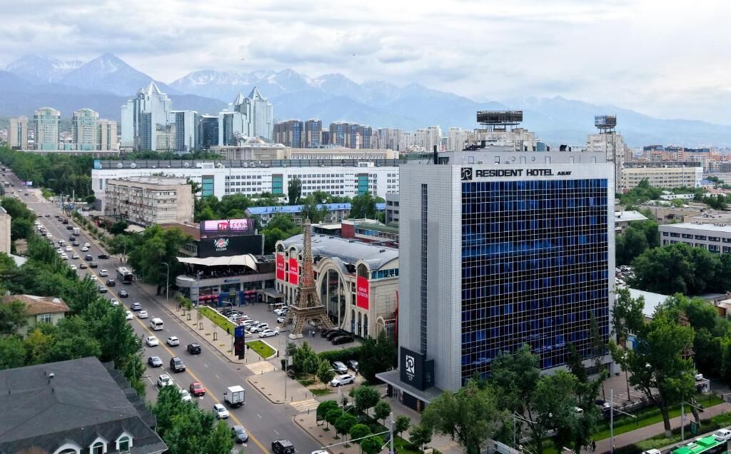 Un hotel con fachada de vidrio moderna, una entrada destacada y vistas a la ciudad y montañas al fondo.