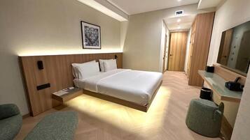 A modern hotel room with a bed, bedside table, chair, and a mirror.