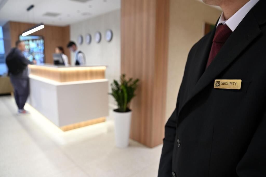 A security guard standing in a hotel lobby with a reception desk and a potted plant.