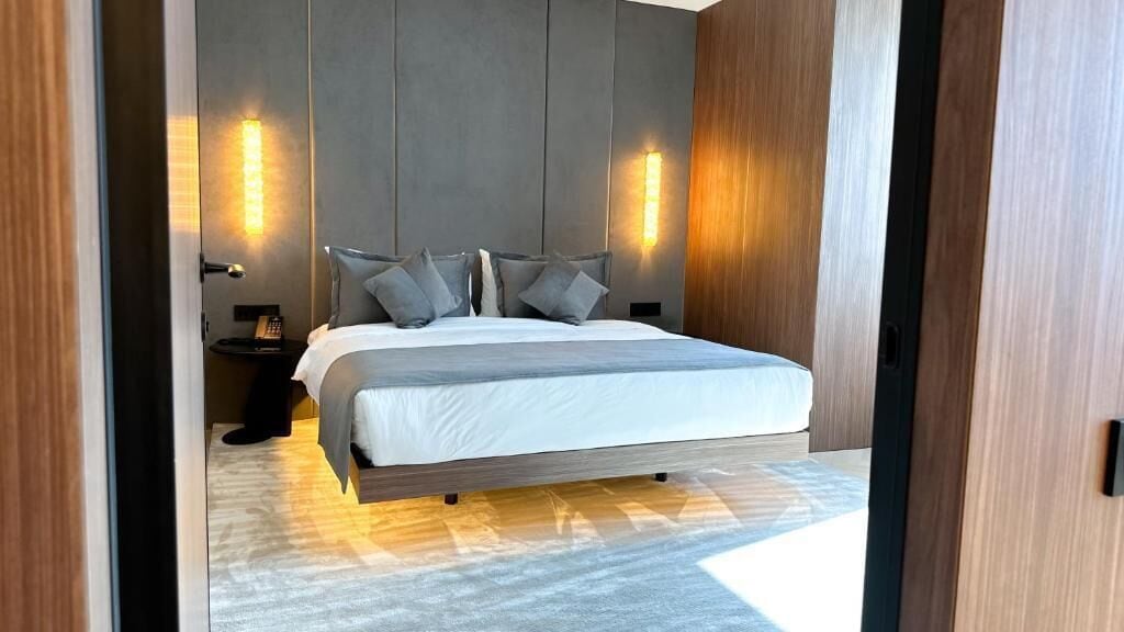 Une chambre à coucher moderne avec un grand lit, des tables de chevet et des lampes fixées au mur.