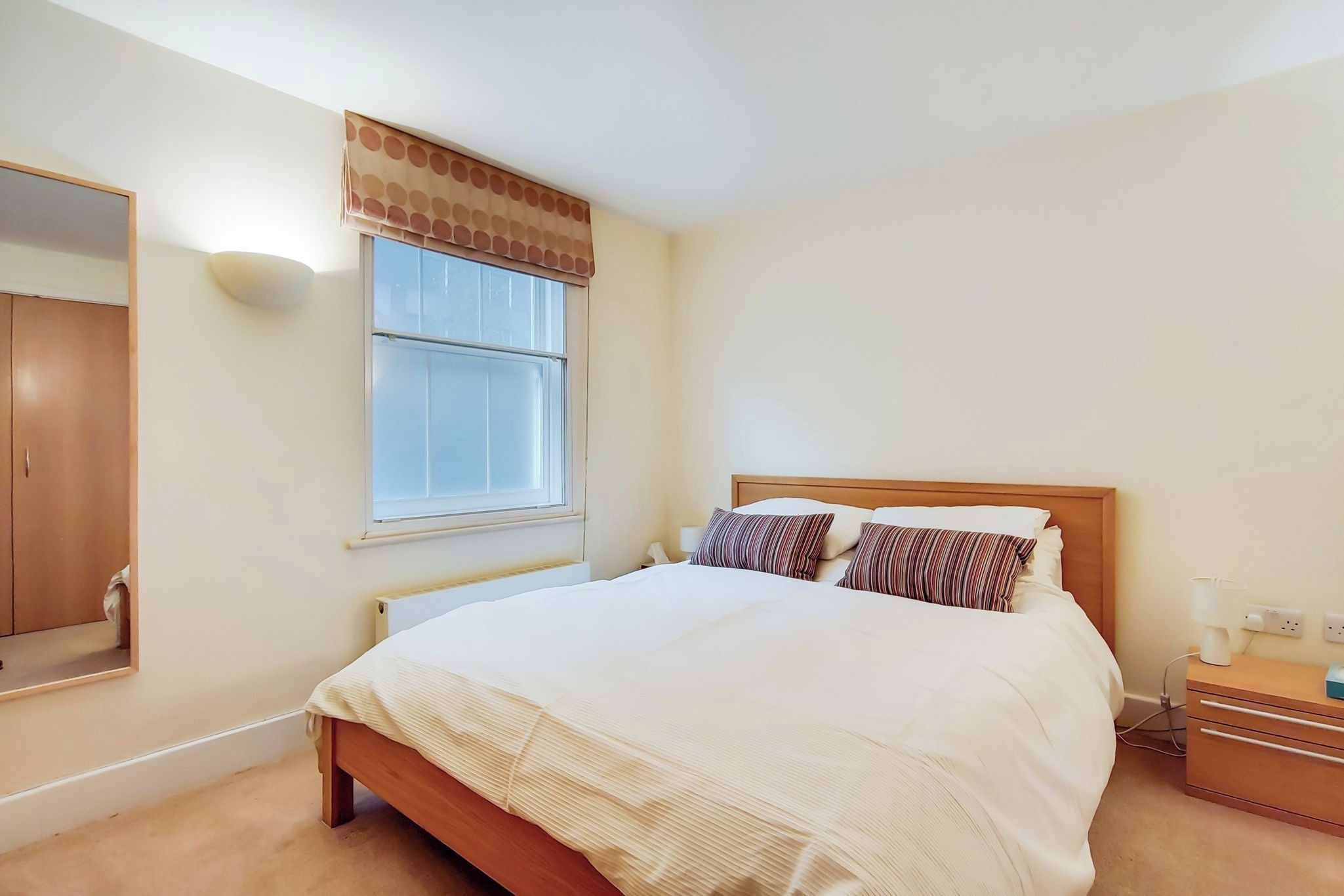 Ein Schlafzimmer mit Bett, Nachttisch, Lampe und einem Fenster mit Jalousien.