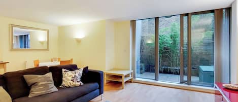 A modern living room with a dark sofa, a small table, and a large sliding glass door leading to an outdoor area.