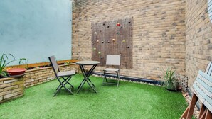 Eine Terrasse mit Backsteinmauer, Holzlattenzaun und einem kleinen Tisch mit Stühlen.