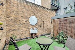 A brick wall with a round blue and white striped sign, a small round table with chairs, and a bamboo fence. - Charming 2BDR London Apt in Kings Cross Sleeps 5 (Greater London)