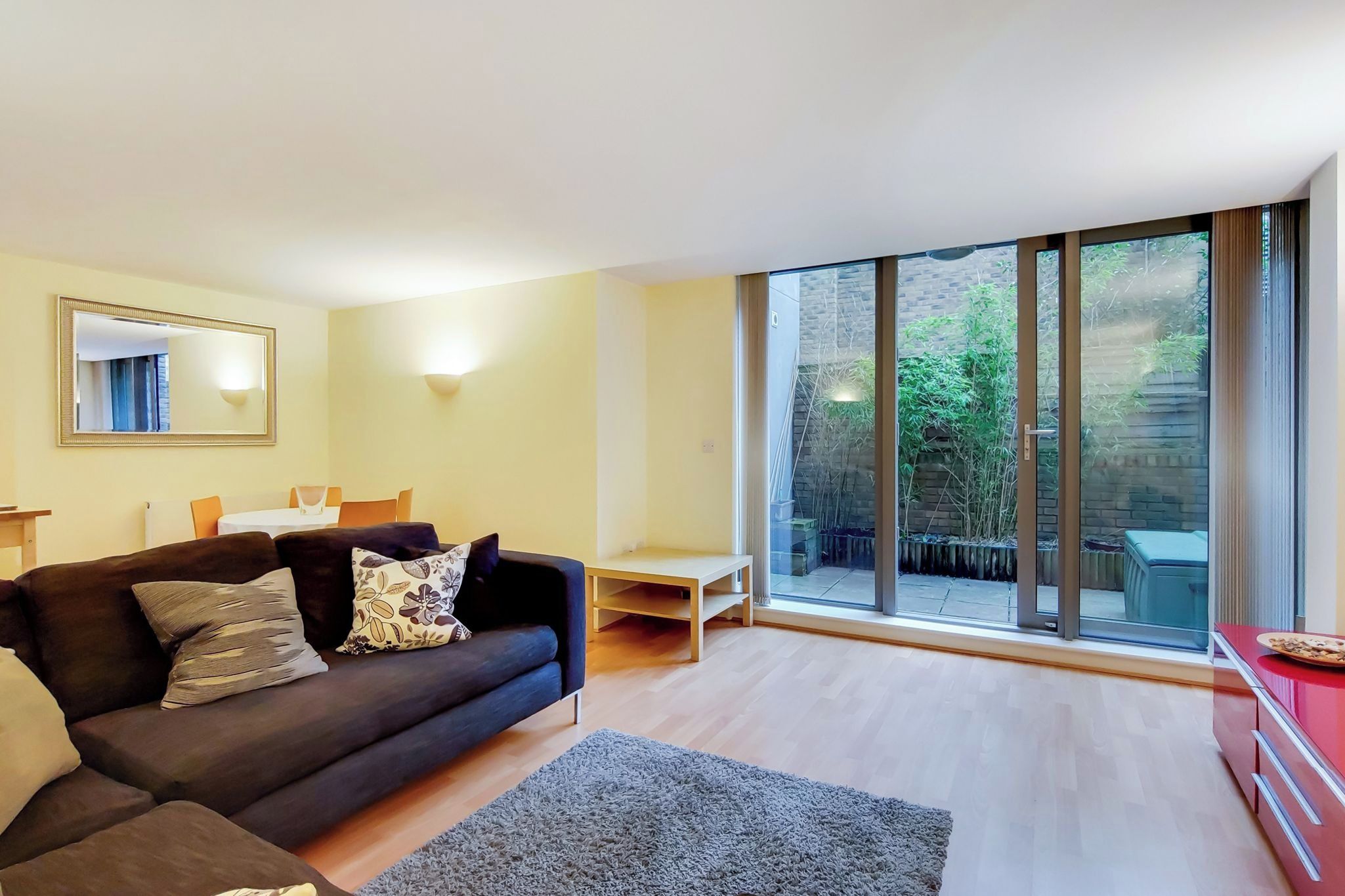 A modern living room with a dark sofa, a small table, and a large sliding glass door leading to an outdoor area.