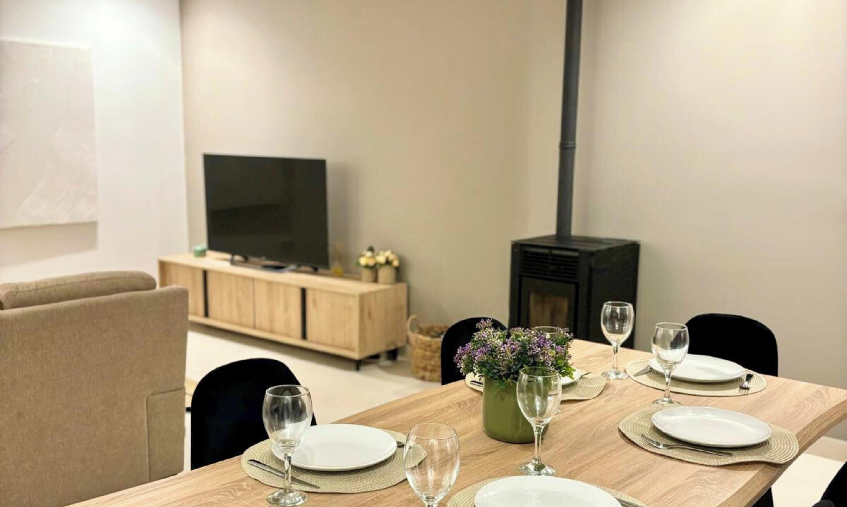 A dining area with a table set for four, a television, and a wood-burning stove.