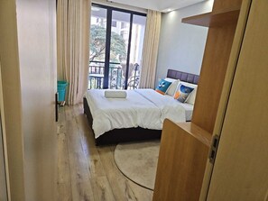 A hotel room with a bed, a window with curtains, a balcony, and a wooden floor. - Siaya Park - Elevate Stay (Kangundo)
