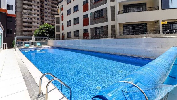 Une piscine à l’eau d’un bleu limpide, une chaise longue au bord de la piscine et un parasol.