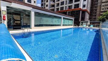 Une piscine à l’eau d’un bleu cristallin, entourée d’un bâtiment moderne aux fenêtres en verre et au toit recouvert de tuiles.