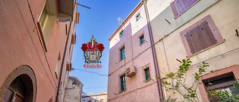 Una estrecha calle flanqueada por edificios, con un camino adoquinado y macetas con plantas.