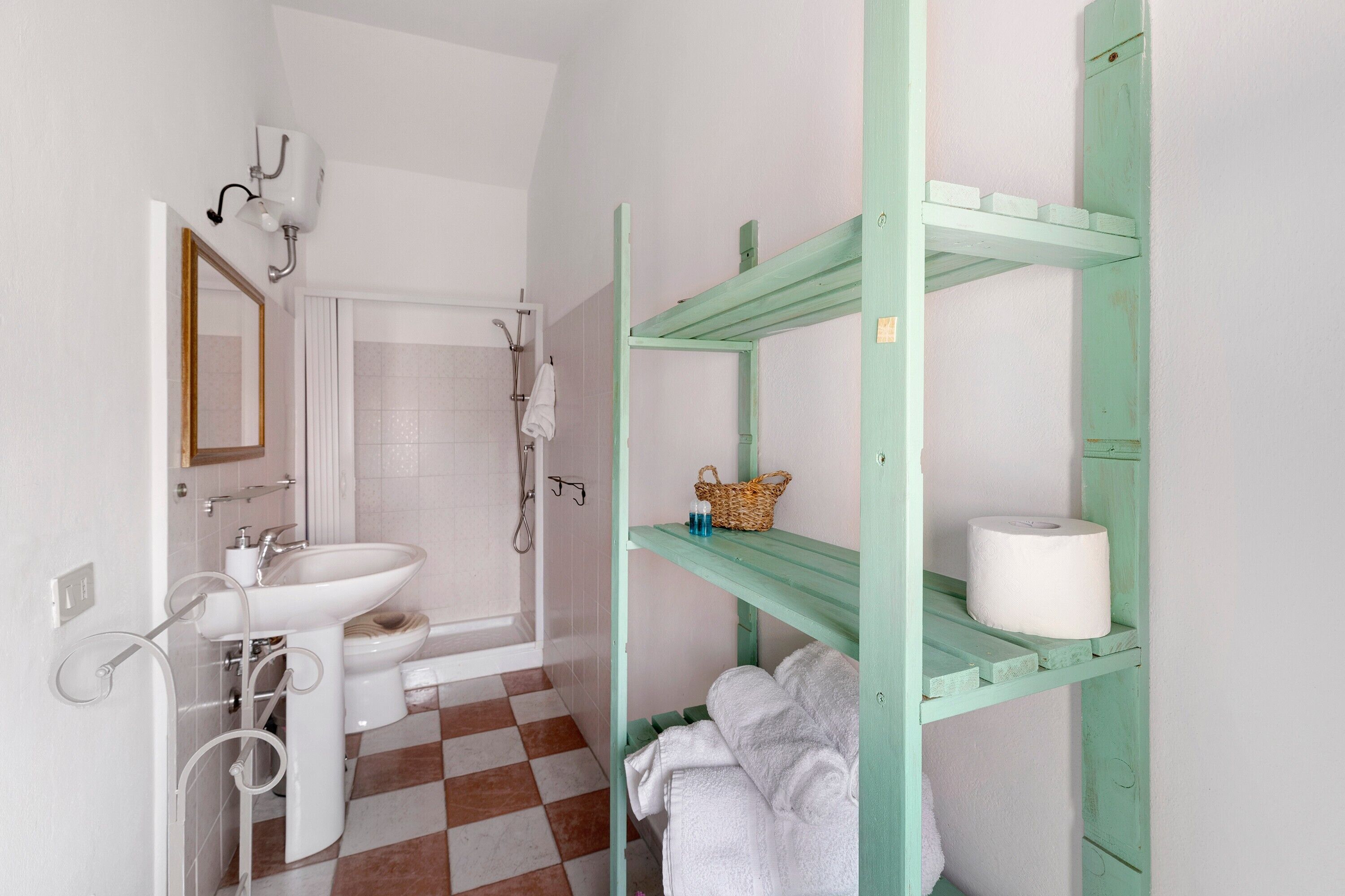 Un bagno con un lavandino bianco, uno specchio, una doccia e un pavimento a scacchi.