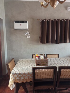 A dining area with a table set for four, a wall-mounted air conditioner, and a curtain.