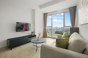 A modern living room with a flat-screen TV, a round coffee table, a sofa, and a large window offering a city view. - Ralen by Kozystay - BSD (Tangerang)