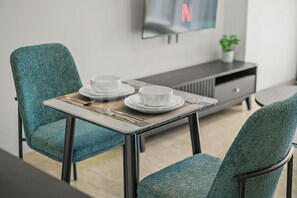 Ein Essbereich mit Tisch für zwei Personen, Stühlen, einem Fernseher und einer kleinen Pflanze auf der Anrichte.