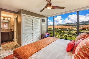 A bedroom with a bed, a ceiling fan, a large window with a view, a closet, and a bathroom with a vanity. - Mahana Resort |  2 Oceanfront Villas, Sleeps 8 | Car Incl. w/ 6+Nights | ML-4190 by KBM (Lahaina)