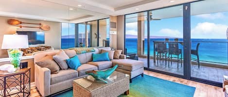A modern living room with a large sofa, a coffee table, and a view of the ocean through large sliding doors.