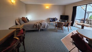 Una habitación de hotel con cama, escritorio, silla, televisor y un ventanal grande.