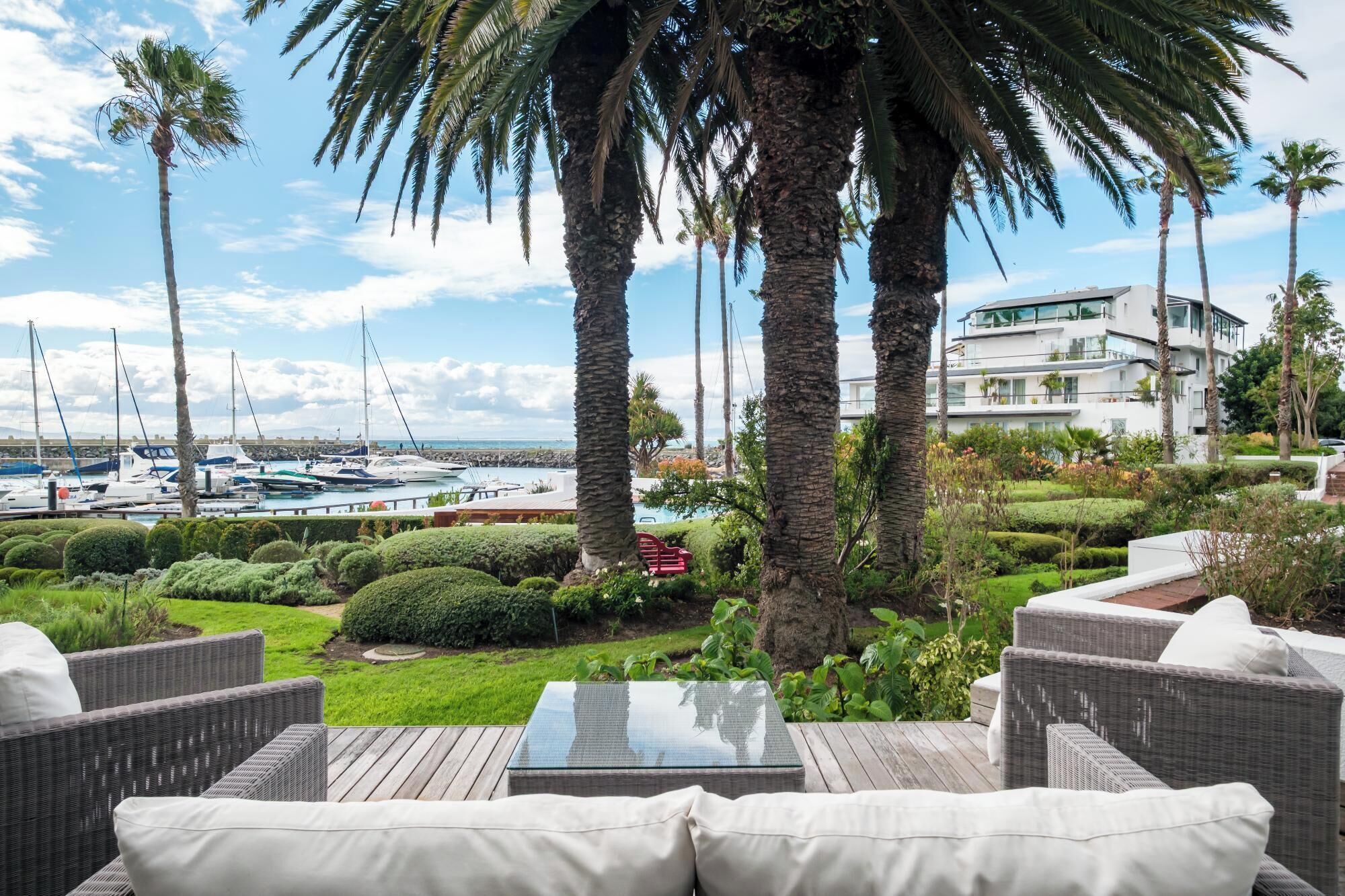 A patio with wicker furniture, a glass-top table, and a view of a marina with boats.