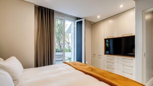 Ein Schlafzimmer mit Bett, Fernseher, einer Holzbank und einer Glastür zum Außenbereich.