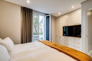 Ein Schlafzimmer mit Bett, Fernseher, einer Holzbank und einer Glastür zum Außenbereich.