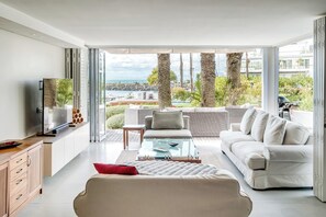 Ein modernes Wohnzimmer mit Sofa, Couchtisch und Fernseher mit Blick auf einen Pool und Palmen.