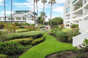 Ein modernes Gebäude mit einem gepflegten Garten, der einen gewundenen Pfad, Palmen und verschiedene Sträucher zeigt.
