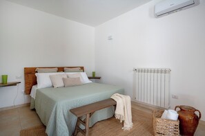 A bedroom with a bed, bedside tables, a bench, a radiator, and a wicker basket. - Beyond the Cones (Puglia)
