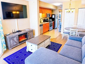 A modern living room with a sofa, coffee table, and fireplace. A kitchen with appliances and a dining area with chairs is visible in the background. - Waterway View Marina Retreat: Harbourgate Marina Club Unit 504 (North Myrtle Beach)