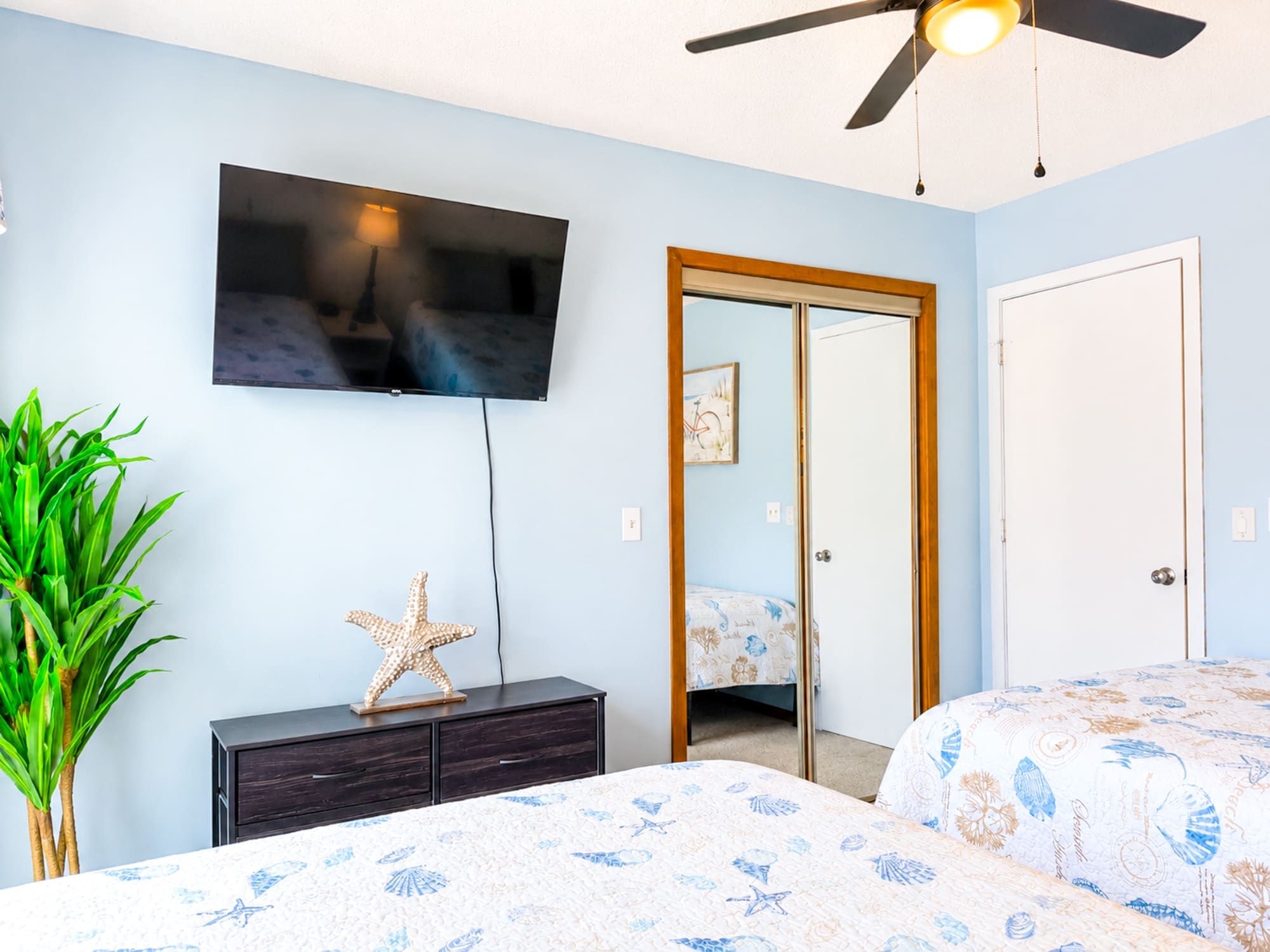 Un dormitorio con cama, cómoda, televisor, ventilador de techo y puerta.